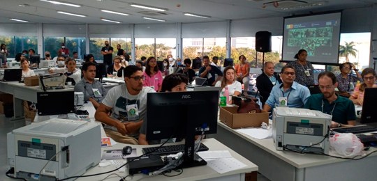 Descrição: imagem de várias pessoas fazendo auditoria em várias urnas eletrônicas.